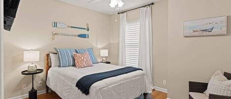 A bedroom with a bed, a ceiling fan, a painting, and a window with curtains.