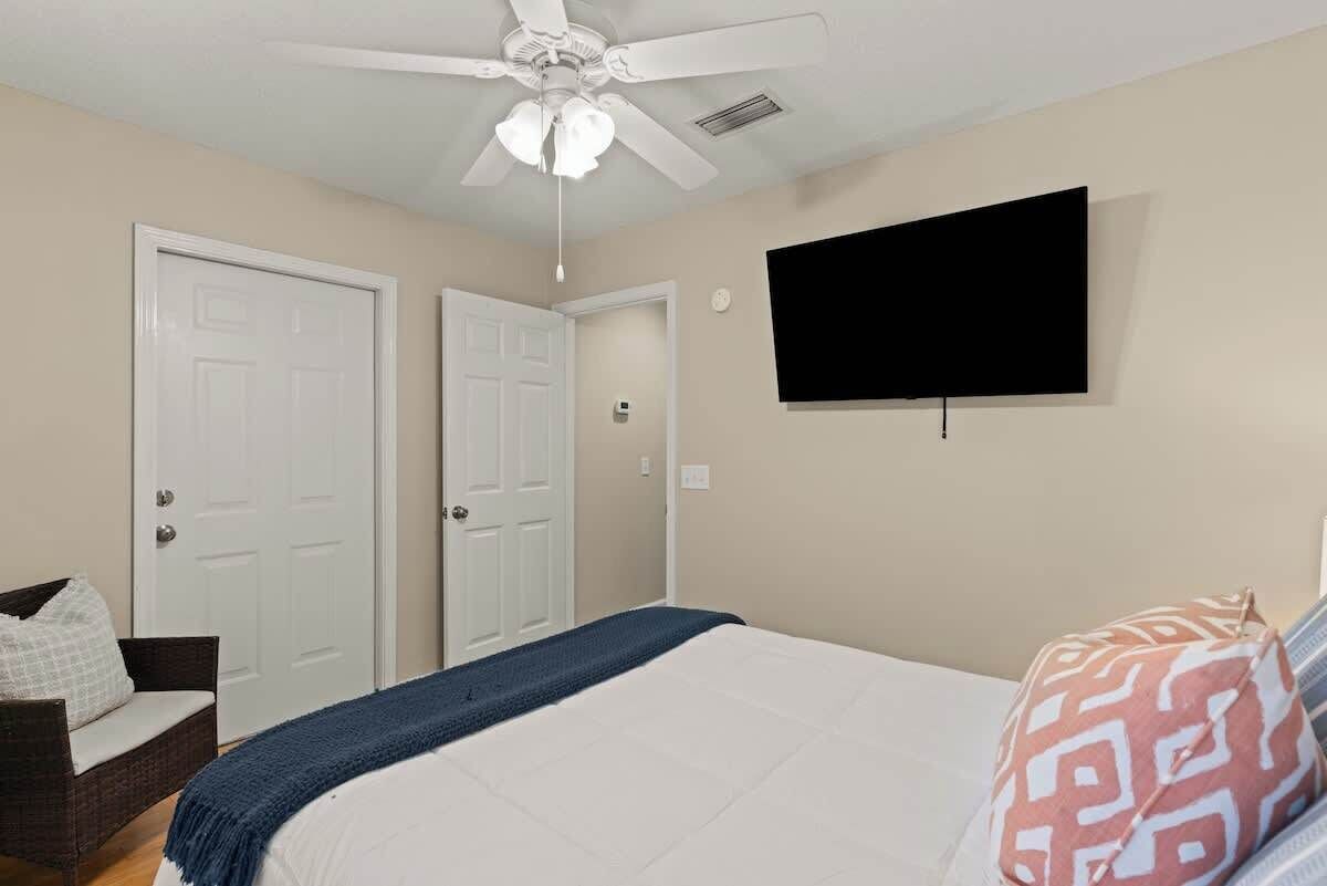 A bedroom with a bed, a ceiling fan, a television, and two doors.