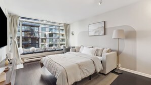 A modern bedroom with a large window, a bed, a floor lamp, and a view of the cityscape.