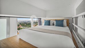 Une chambre d’hôtel moderne avec un grand lit, une vue sur la ville et une porte coulissante donnant sur le balcon.
