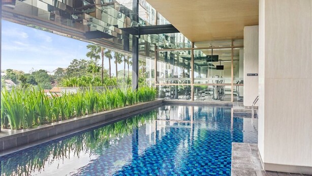 Une piscine intérieure moderne aux murs de verre, entourée de verdure et offrant une vue sur le paysage urbain.
