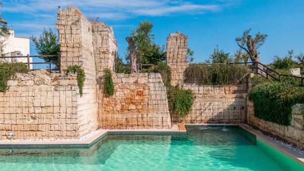 Une piscine à l’eau turquoise et limpide, entourée de murs de pierre et de végétation.