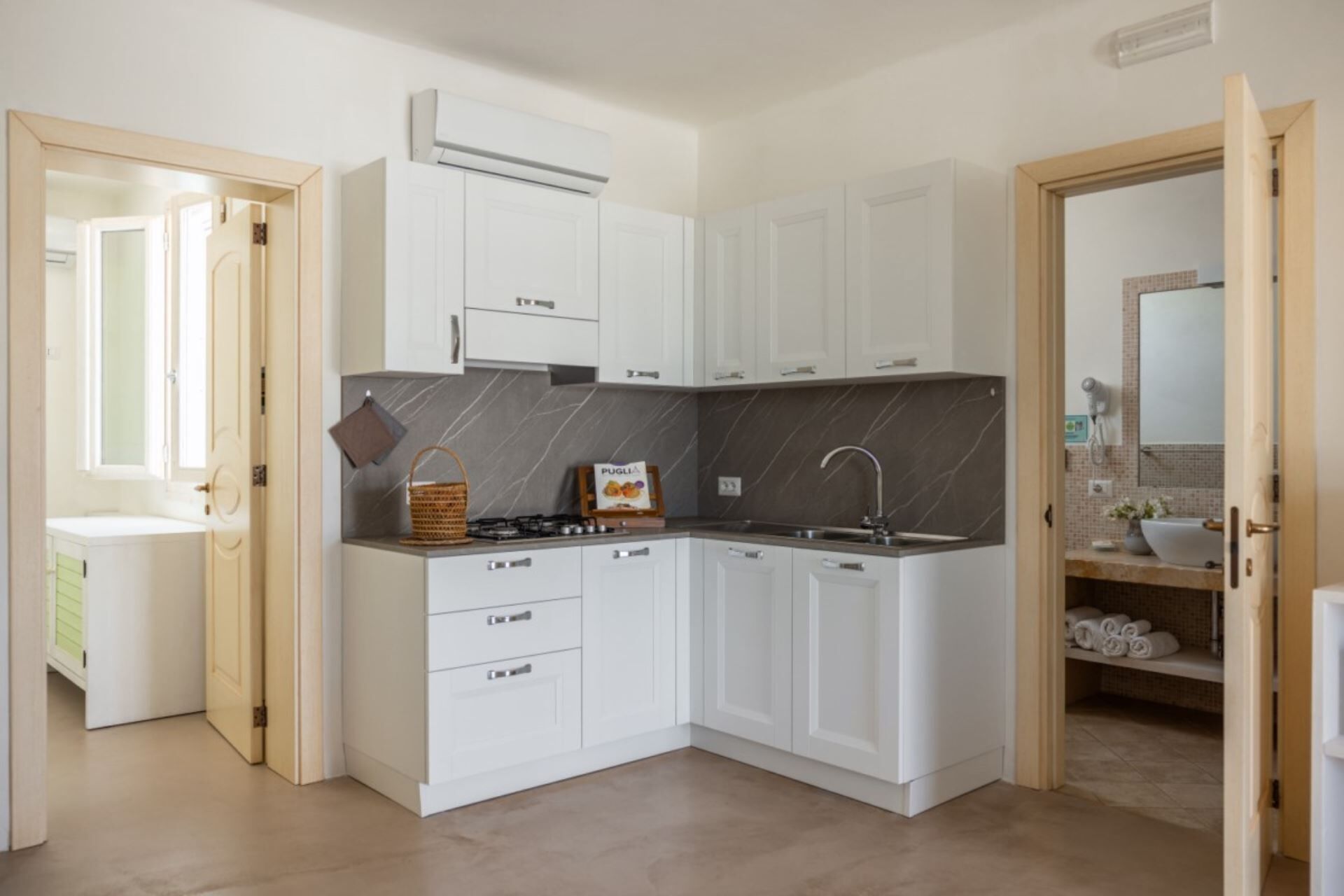 Une cuisine compacte avec des meubles blancs, une cuisinière à gaz et un dosseret en marbre.