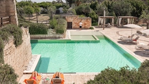 A rectangular swimming pool with clear water, surrounded by a stone wall and lush greenery. There are lounge chairs and a small structure with a person standing nearby. - Cava Li Santi Residence - Monolocale 2 Int 11 (Santa Caterina)