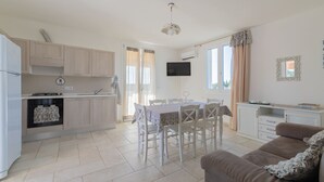 Una cocina moderna con armarios blancos, una mesa de comedor con sillas, un sofá y un televisor montado en la pared.
