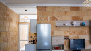 Une cuisine compacte avec un mur en pierre, un réfrigérateur, une télévision et un petit coin repas.