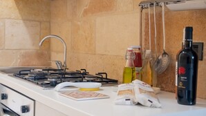 Une cuisine équipée d’une cuisinière à gaz, d’un évier et de divers ustensiles, notamment une bouteille d’huile d’olive, une bouteille de vin rouge et un sac de farine.