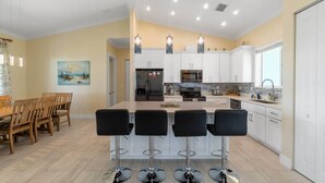 A modern kitchen with white cabinets, a central island with bar stools, and pendant lighting.