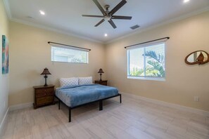 A bedroom with a bed, two nightstands, a ceiling fan, and two windows with blinds.