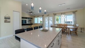 A spacious kitchen with a large island, a dining area with a wooden table and chairs, and a ceiling fan.