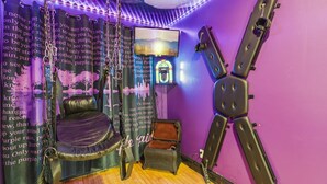 A room with a purple wall, a hanging chair, a small chest, and a guitar.