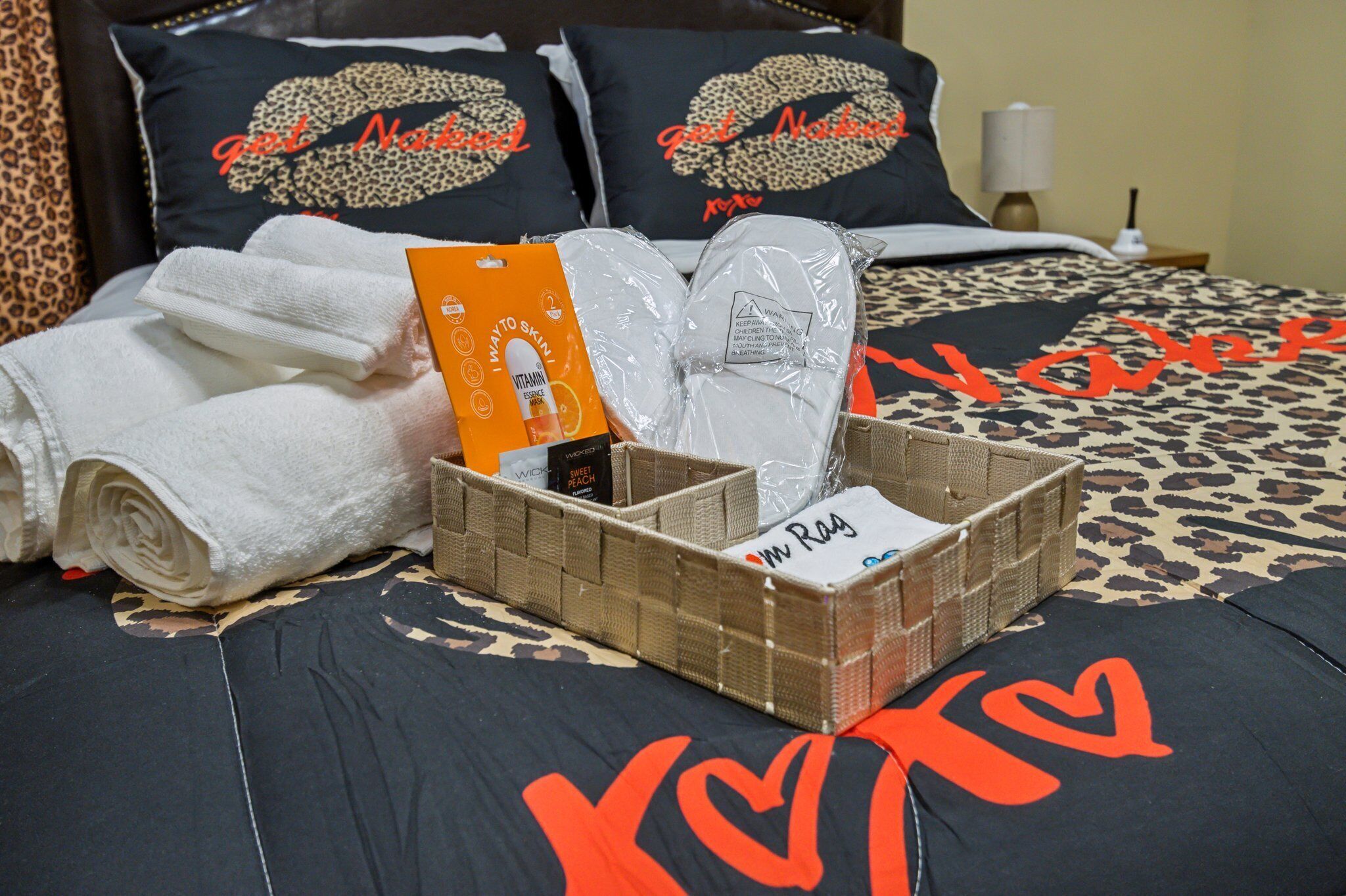 A neatly made bed with a leopard print bedspread and pillows with a heart design. There are rolled white towels, a basket with toiletries, and a box of lotion.