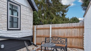 A patio with a wooden fence, a metal table and chairs, and a window with a view of trees.
