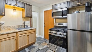 A modern kitchen with dark wooden cabinets, a stainless steel refrigerator, a built-in oven, a microwave, and a gas stove.