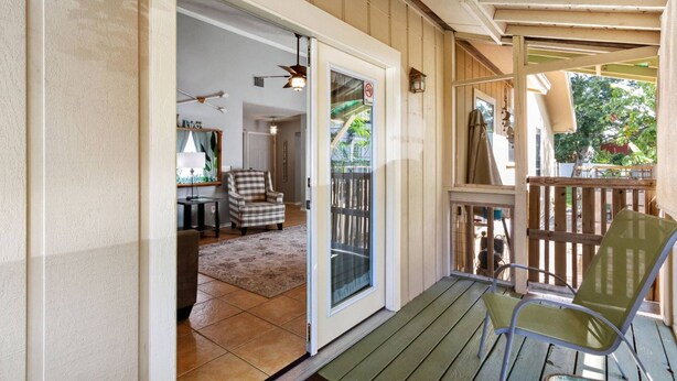 A covered porch with a wooden deck, a green chair, and a sliding glass door leading to an interior room with a chair and a table. - 3BR Turtle Hut - Beach House w/ Fenced Yard & Firepit (Jacksonville Beach)