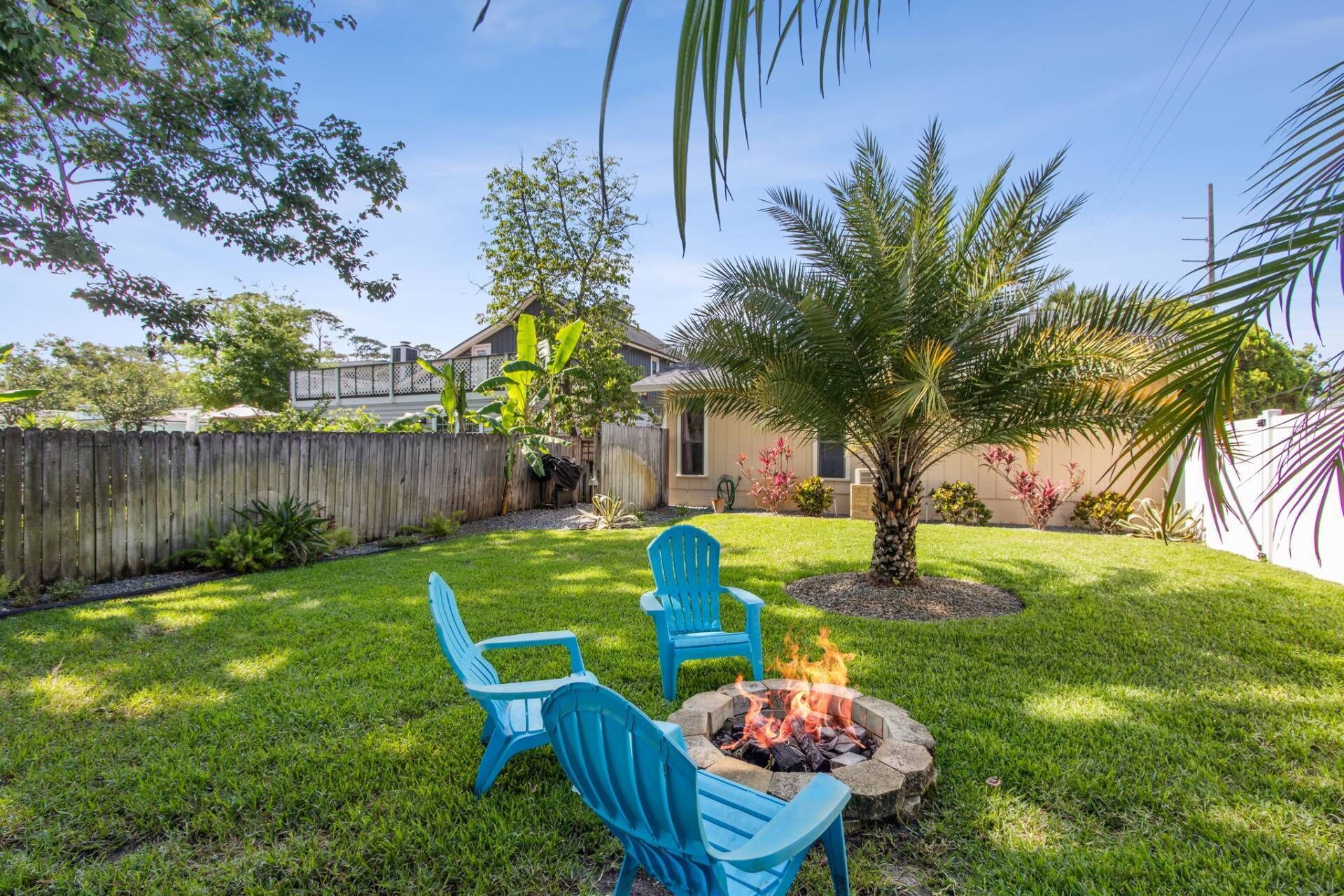 A backyard with a fire pit, two blue chairs, and a small tree.