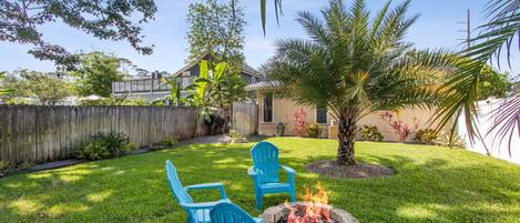 A backyard with a fire pit, two blue chairs, and a small tree.