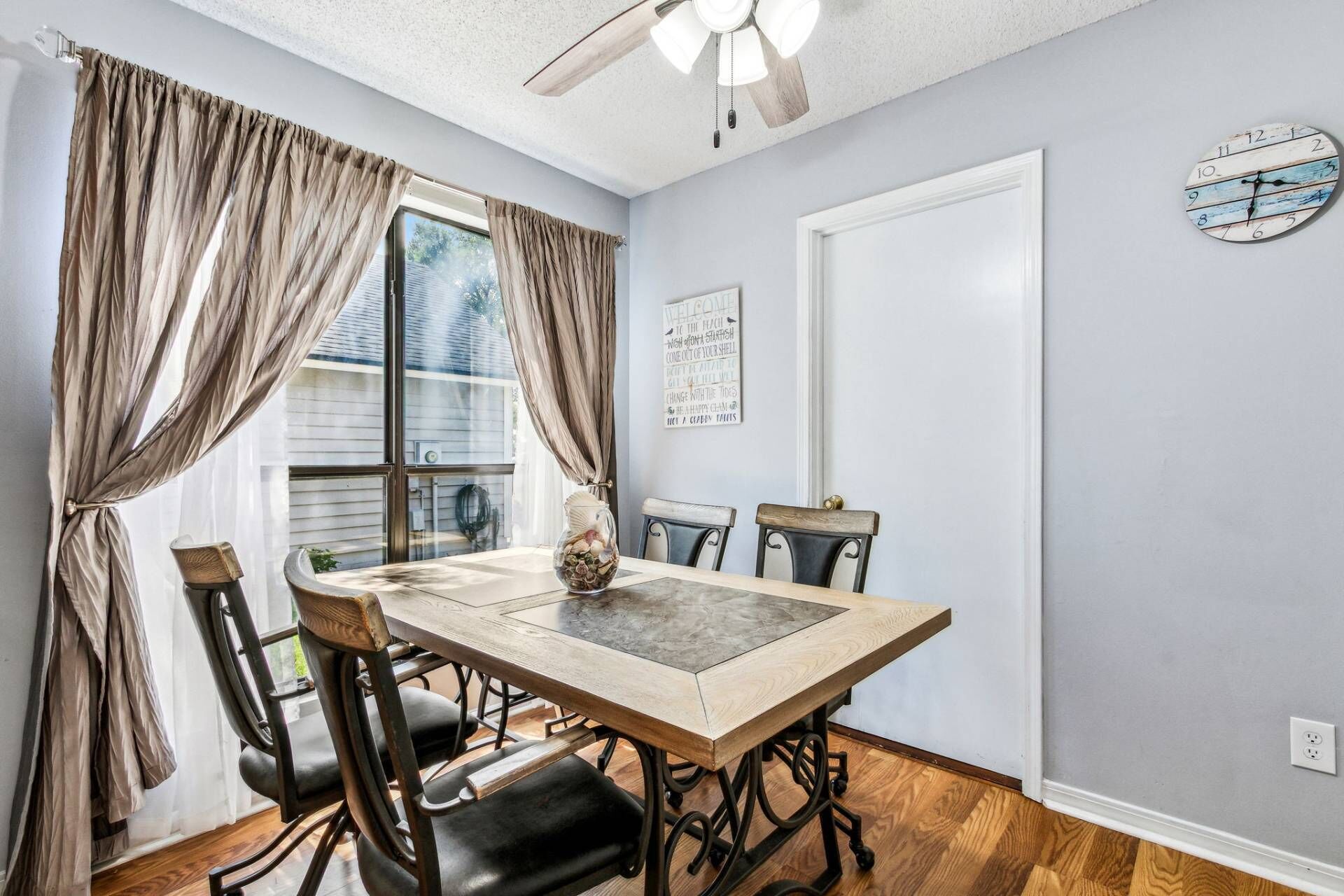 A dining room with a wooden table, black chairs, a ceiling fan, and a wall clock.