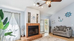A living room with a fireplace, a sofa, and nautical-themed wall decor. - 3BR Turtle Hut - Beach House w/ Fenced Yard & Firepit (Jacksonville Beach)