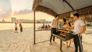 A beachside barbecue setup with a city skyline in the background. - Vinhomes Ocean Park- Luxury Apartments (Hanoi)