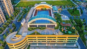 A modern hotel with a curved parking structure, a central swimming pool, and landscaped areas. - Vinhomes Ocean Park- Luxury Apartments (Hanoi)