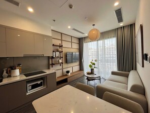 A modern living room with a sofa, a dining table, and a kitchen area with a TV. - Solvira Ocean Park Residency (Gia Lam)