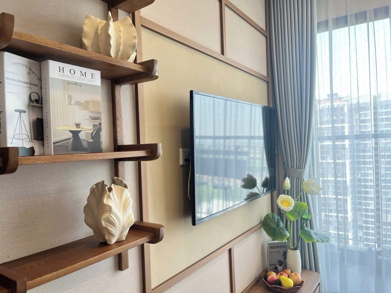 A modern living room with a mounted TV, wooden shelves, and a vase with flowers.