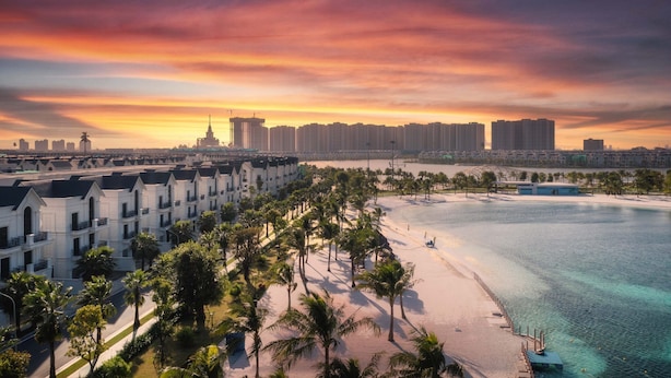 A coastal hotel with a beachfront view, palm trees, and a city skyline in the background. - Vinhomes Ocean Park- Luxury Apartments (Hanoi)