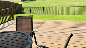 Une terrasse en bois avec deux fauteuils en osier et une vue sur un champ verdoyant et des arbres.