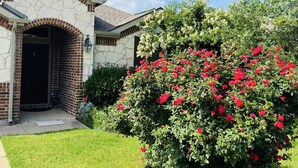 Une maison avec une façade en pierre, une arche en briques et un jardin bien entretenu agrémenté de fleurs rouges.