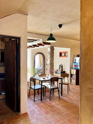 Un comedor con un pilar de piedra, sillas de madera, una mesa y una lámpara colgante verde.