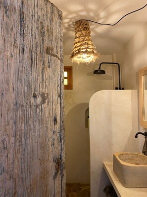 Un baño rústico con pared de madera, lavabo de piedra y una lámpara colgante.