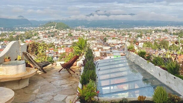 A rooftop terrace with a view of a cityscape, stone flooring, and a small seating area with a table and chairs.