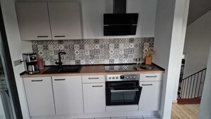 A compact kitchen with white cabinets, a black oven, a coffee maker, and a tiled backsplash.