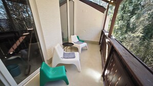 A balcony with two white plastic chairs and a green plastic chair, a small round table, and a wooden railing.