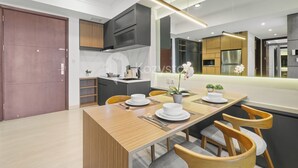 A modern kitchen with a wooden dining table set for two, a built-in oven, and a large window. - Solaya by Kozystay - Kuningan (Jakarta)