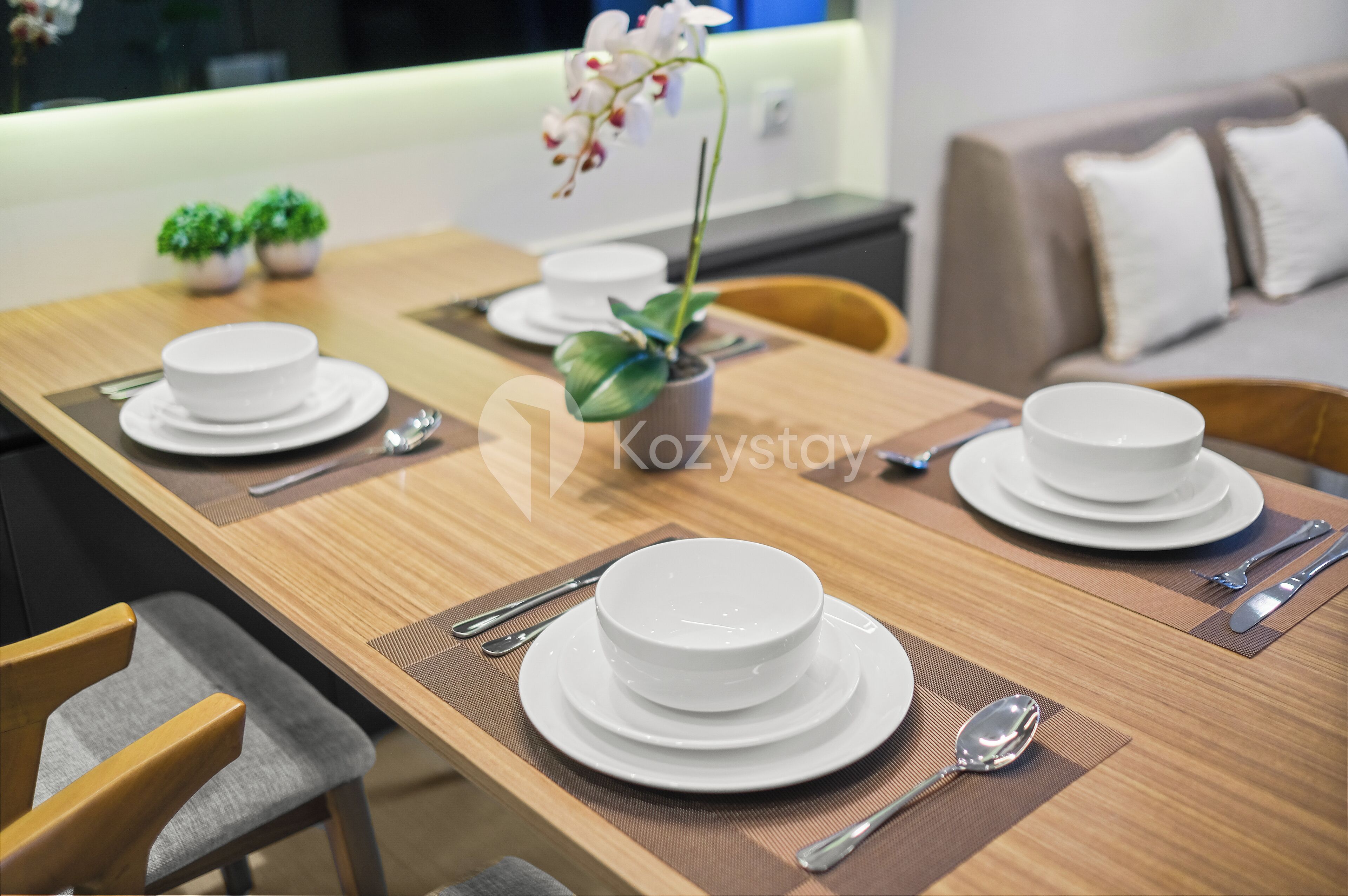 A dining table set with white plates, silverware, and a potted orchid.