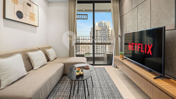 A modern living room with a sofa, a coffee table, a flat-screen TV, and a balcony with a city view. - Solaya by Kozystay - Kuningan (Jakarta)