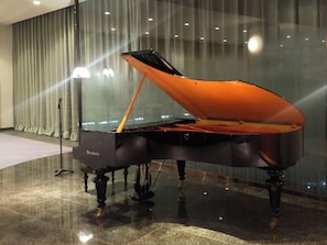 A grand piano in a spacious, well-lit room with a reflective floor and a large window with curtains. - Karuizawa Club of Art (Karuizawa)