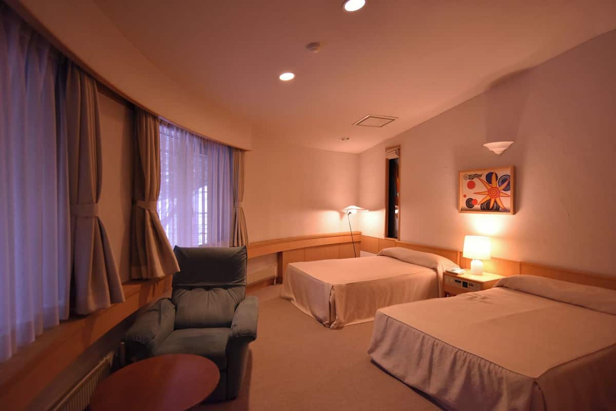 A hotel room with two beds, a chair, a table, and a painting on the wall.
