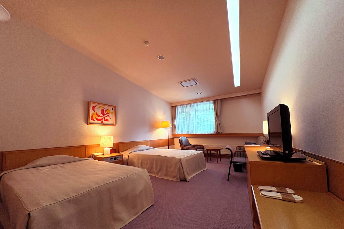 A hotel room with two beds, a desk with a computer, a chair, and a TV.