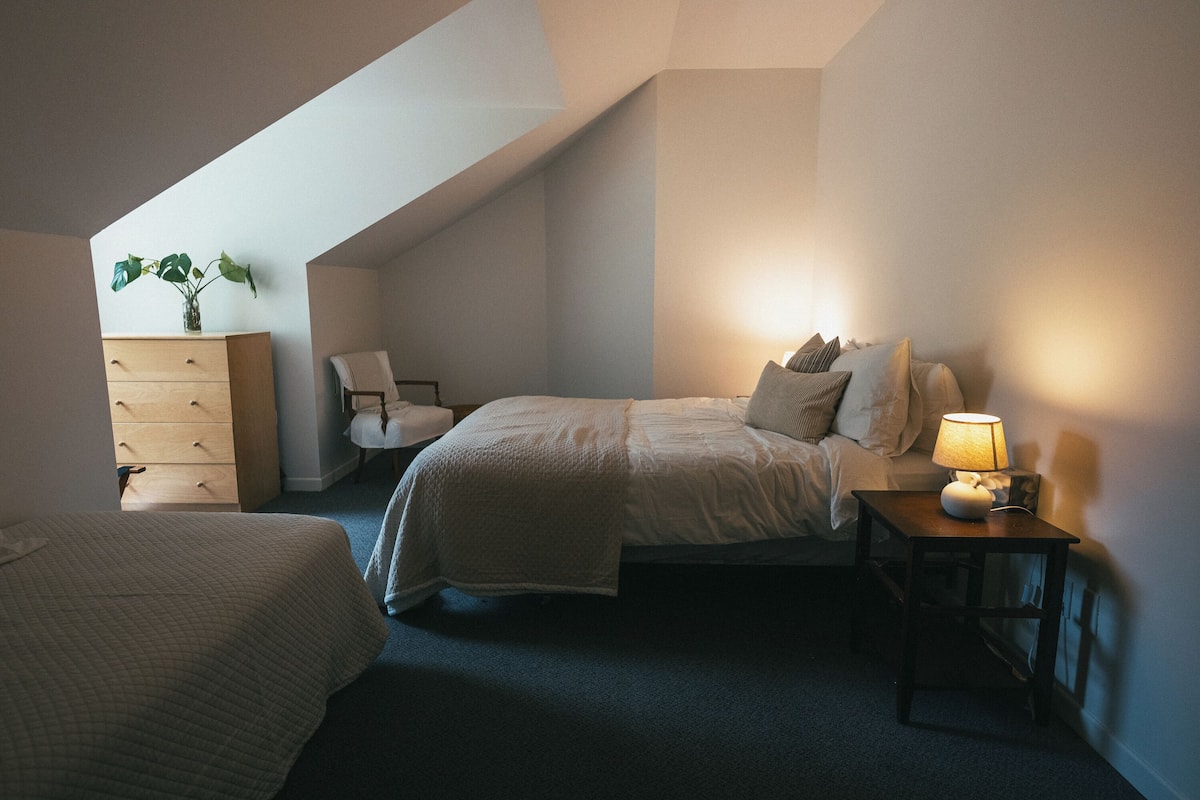 A bedroom with a bed, bedside table with a lamp, a chair, a dresser, and a plant.