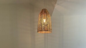 A neatly made bed with a white quilt, a geometric-patterned pillow, and a hanging woven light fixture above. - MacTaverne (Val-David)