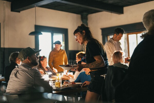 A restaurant with patrons seated at tables, a server attending to guests, and a bar area visible in the background. - MacTaverne (Val-David)