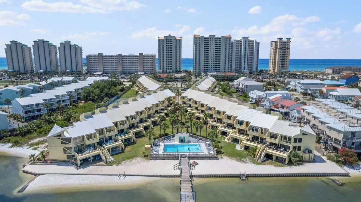 A resort with multiple buildings, a central pool, and a beach view.