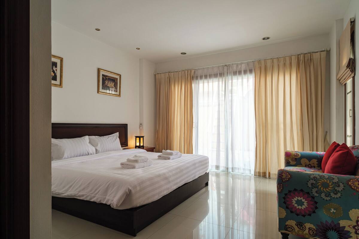 A hotel room with a large bed, a sofa, and a window with curtains.