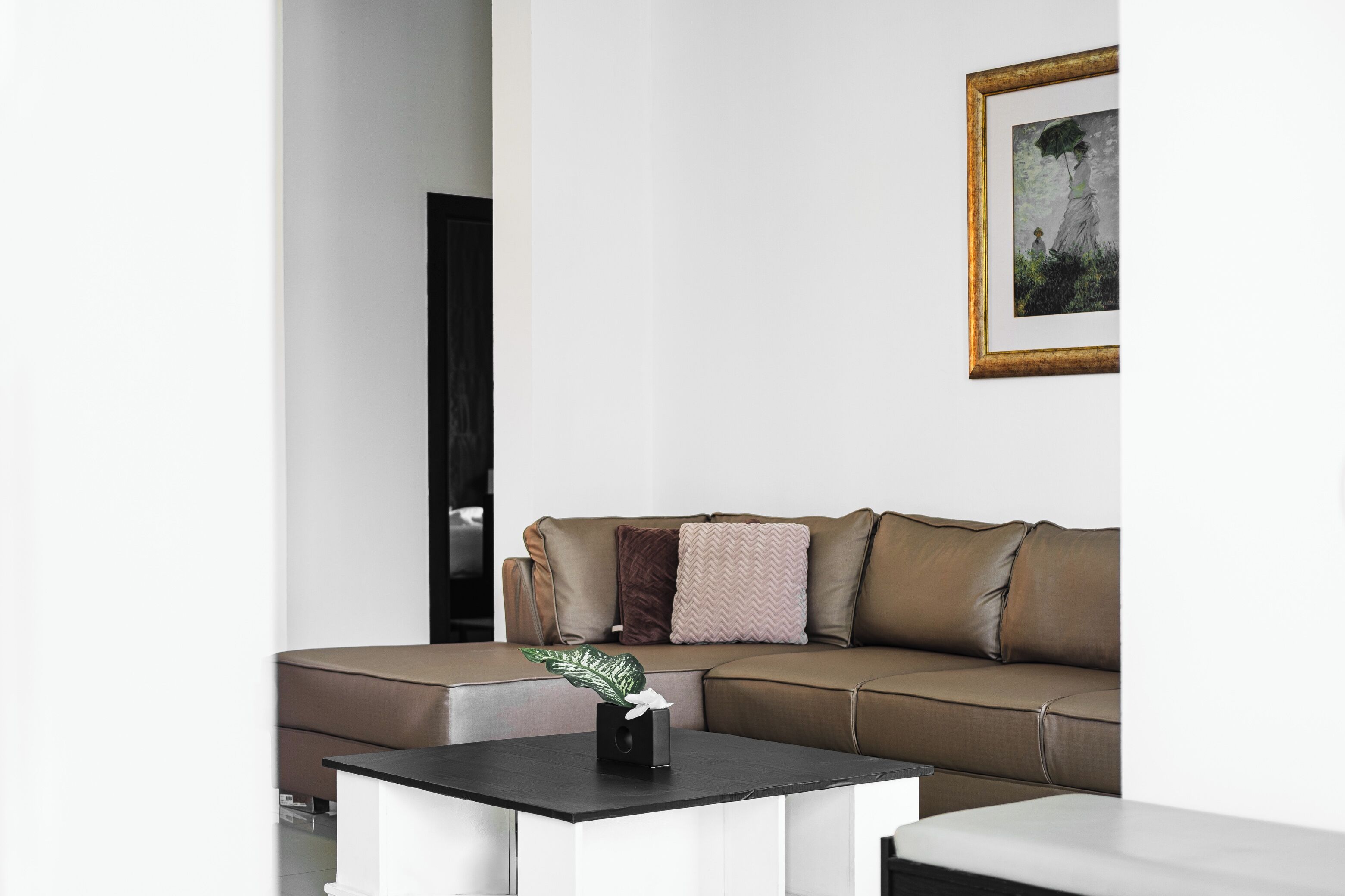 Una sala de estar moderna con un sofá de cuero marrón, una mesa de centro negra y una obra de arte enmarcada en la pared.