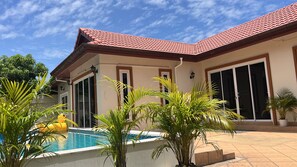 Una propiedad residencial con piscina, palmeras y techo de tejas rojas.