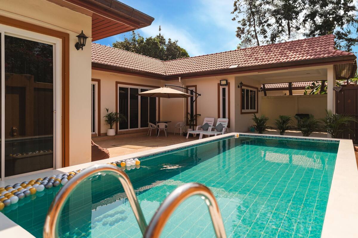 A swimming pool with a tiled deck, lounge chairs, and a pergola.