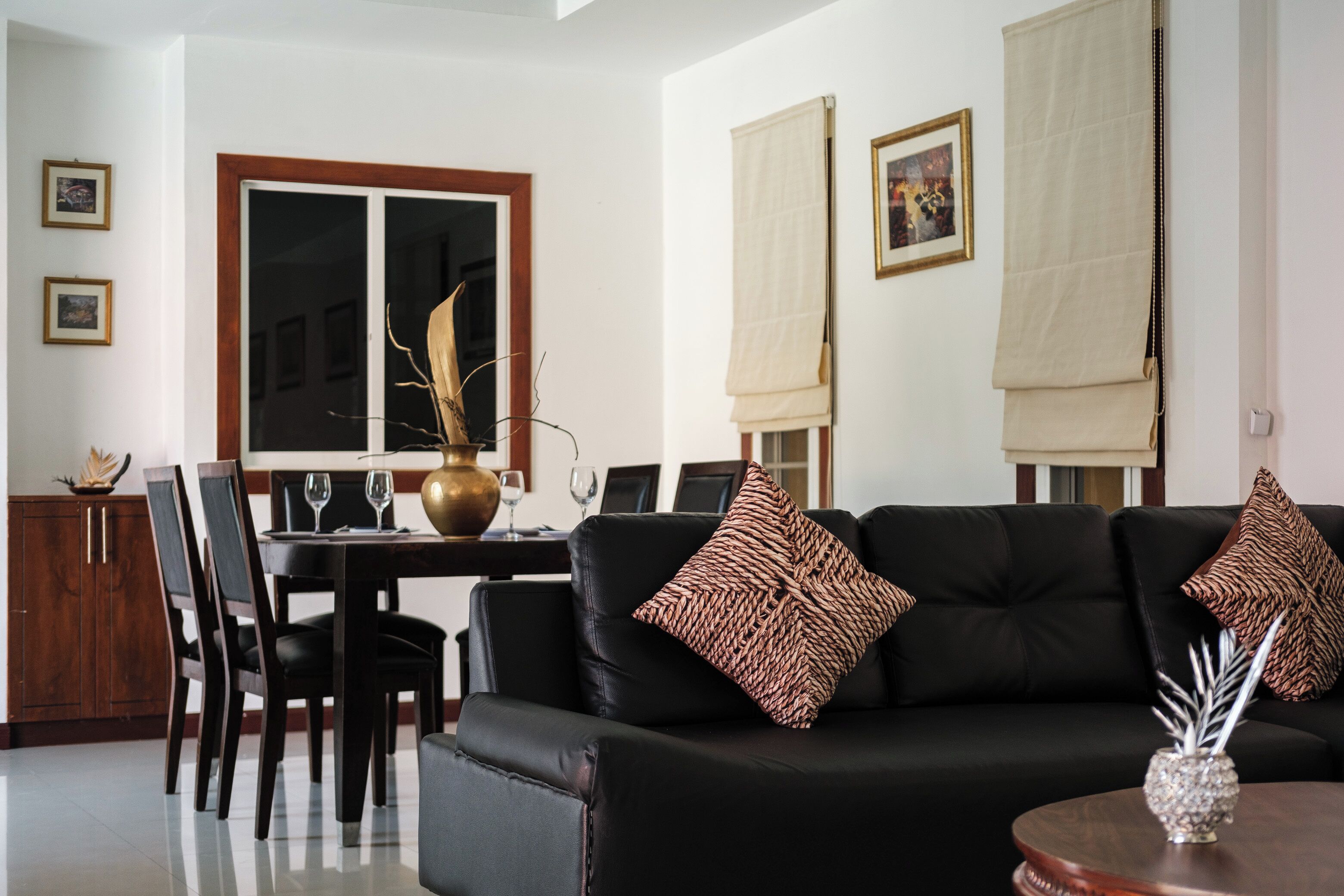 Un salon moderne avec un canapé en cuir noir, une table à manger avec des chaises et un vase décoratif posé sur une table d’appoint.